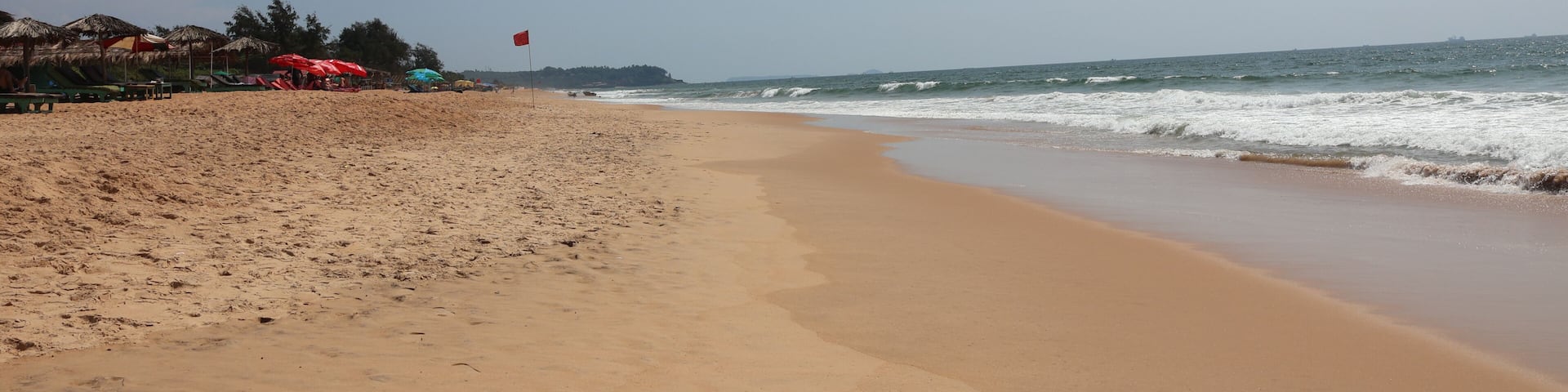 A sandy beach with umbrellas and a flag, ocean waves, and a clear sky.
