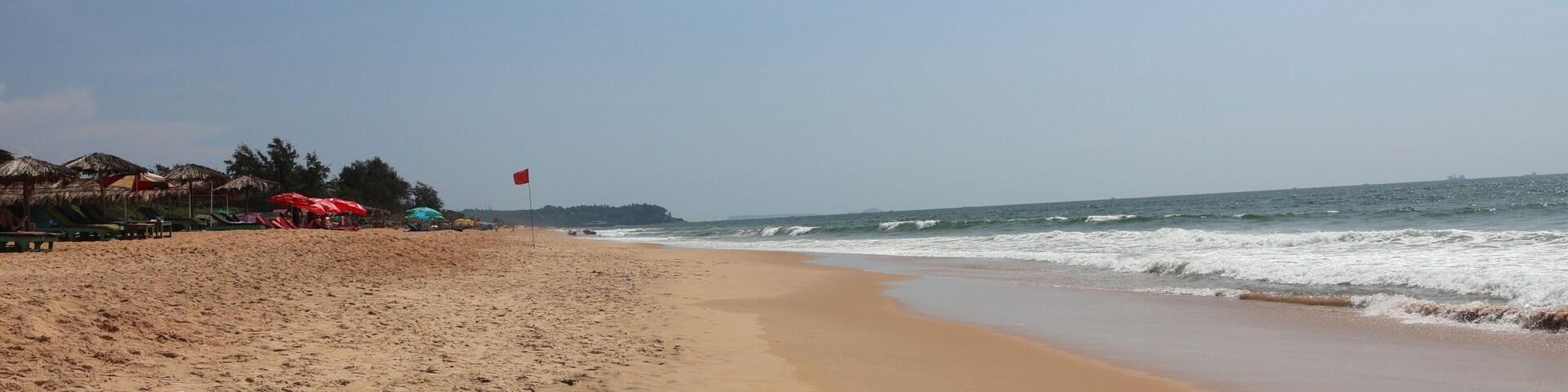 A sandy beach with umbrellas and a flag, ocean waves, and a clear sky.