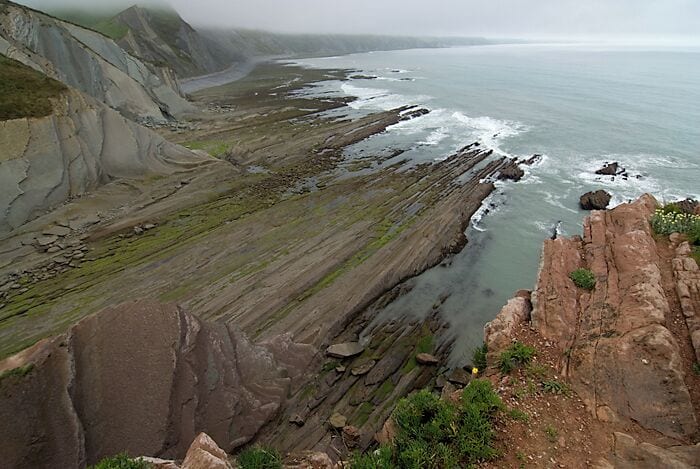 A coastal landscape with layered rock formations and a rugged coastline.