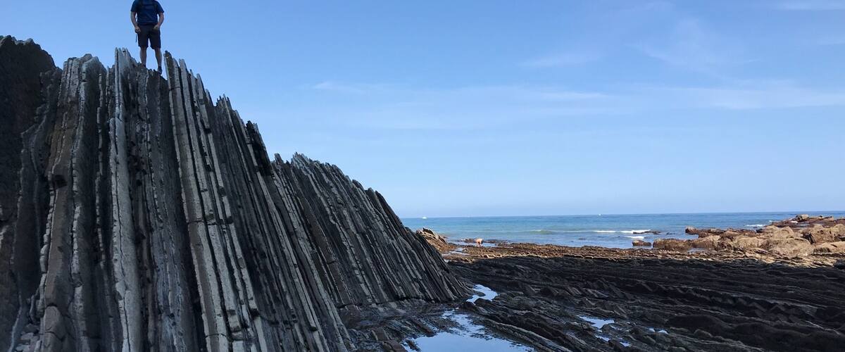 A person standing on a steep, rocky cliff with a body of water at the base.