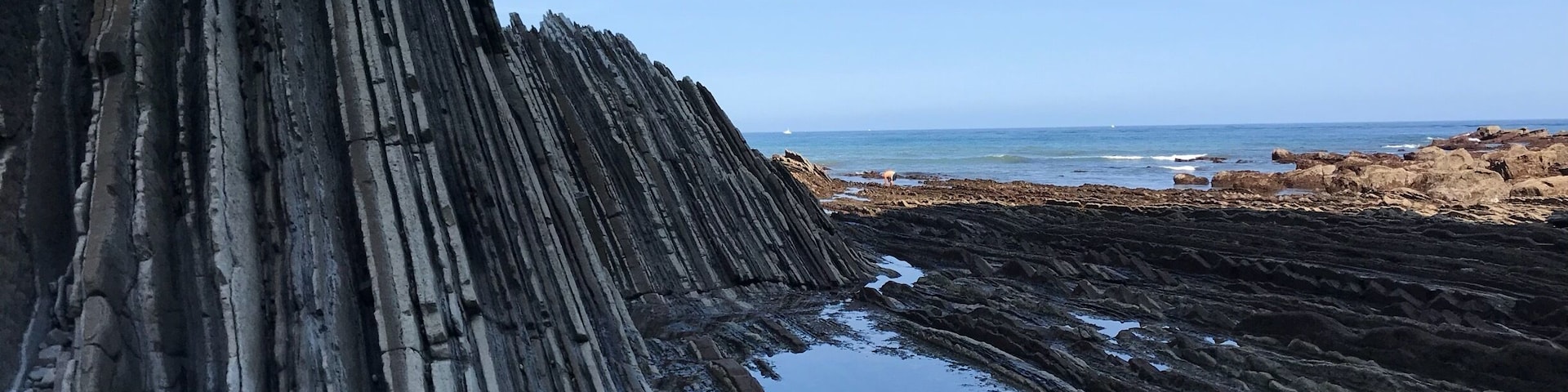 A person standing on a steep, rocky cliff with a body of water at the base.