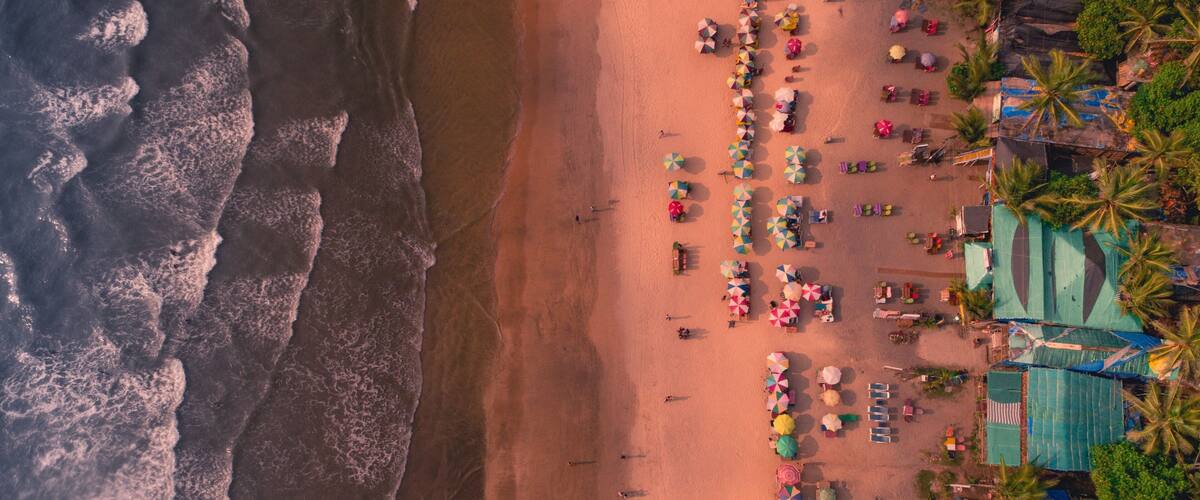 An aerial view of a beach with waves, umbrellas, and palm trees.