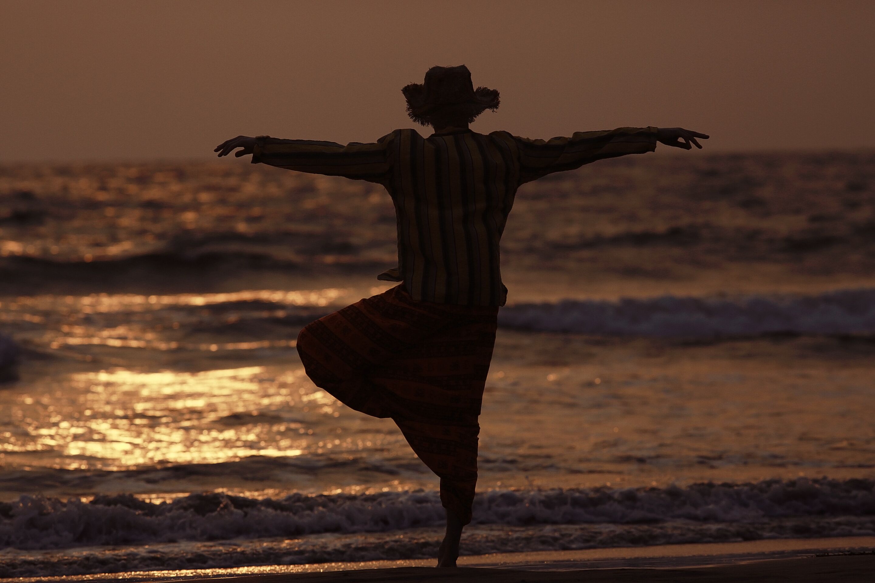 Uma pessoa dançando na praia ao pôr do sol.