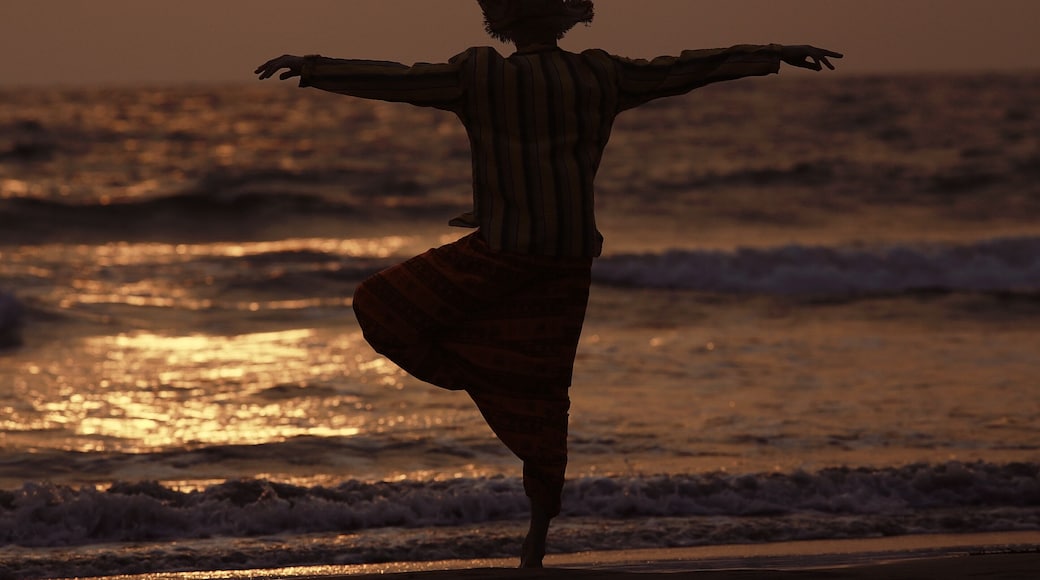 Uma pessoa dançando na praia ao pôr do sol.