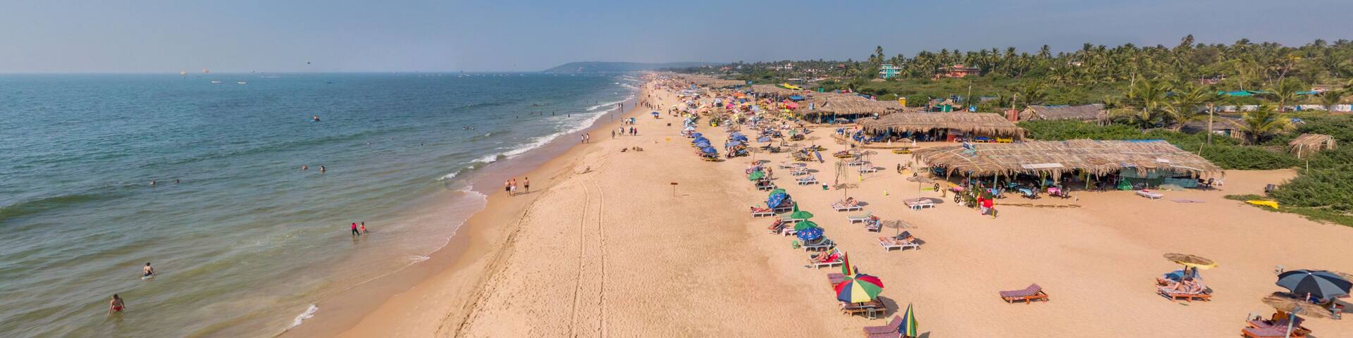 A wide sandy beach with thatched-roof huts and colorful umbrellas along the shoreline.