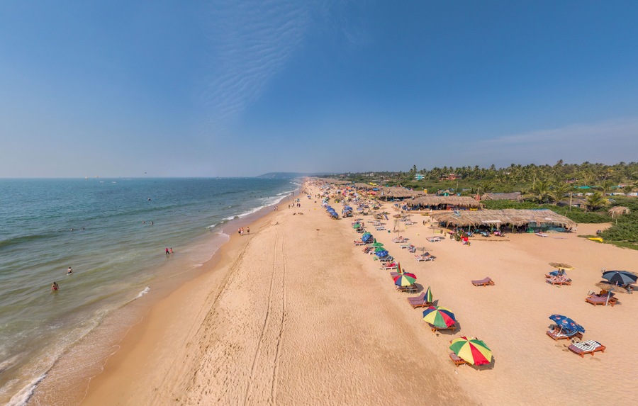 Una extensa playa de arena con cabañas de techo de paja y sombrillas de colores a lo largo de la orilla.