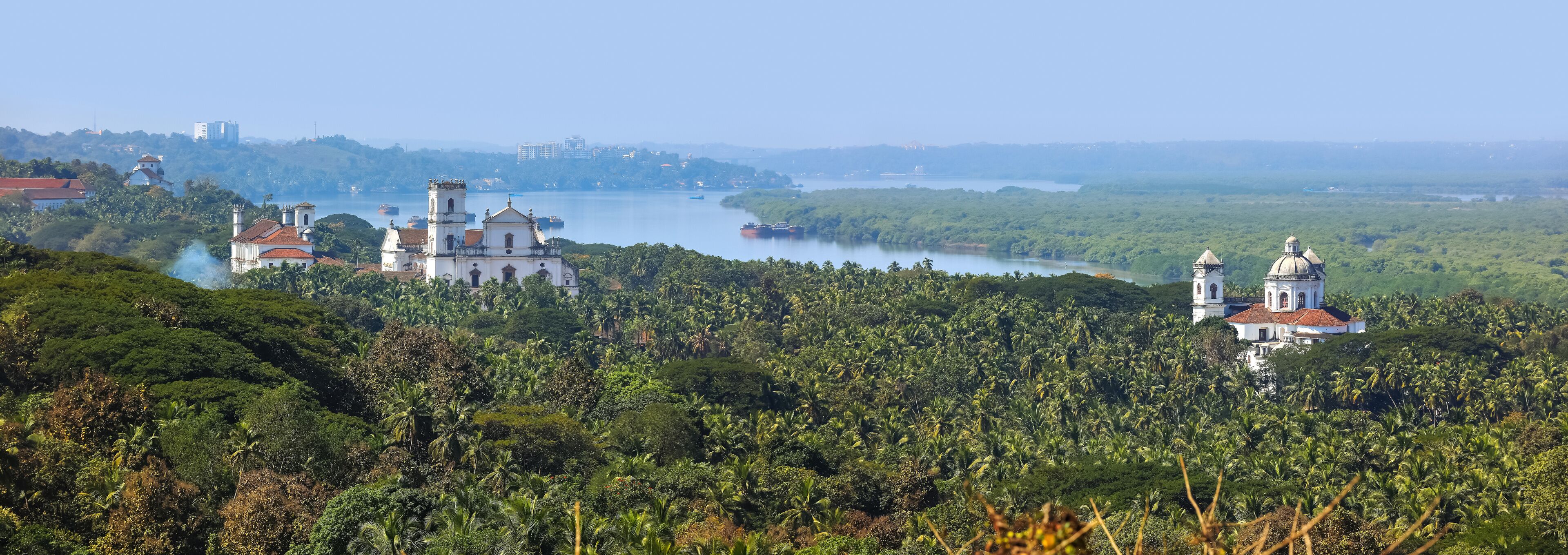 A lush green landscape with a river, a white church with a bell tower, and a dome-roofed building.