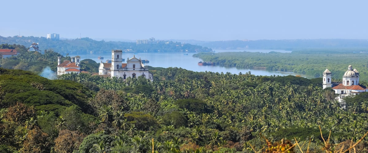 A lush green landscape with a river, a white church with a bell tower, and a dome-roofed building.