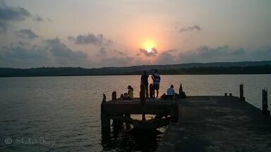 A sunset over a calm lake with people on a dock.