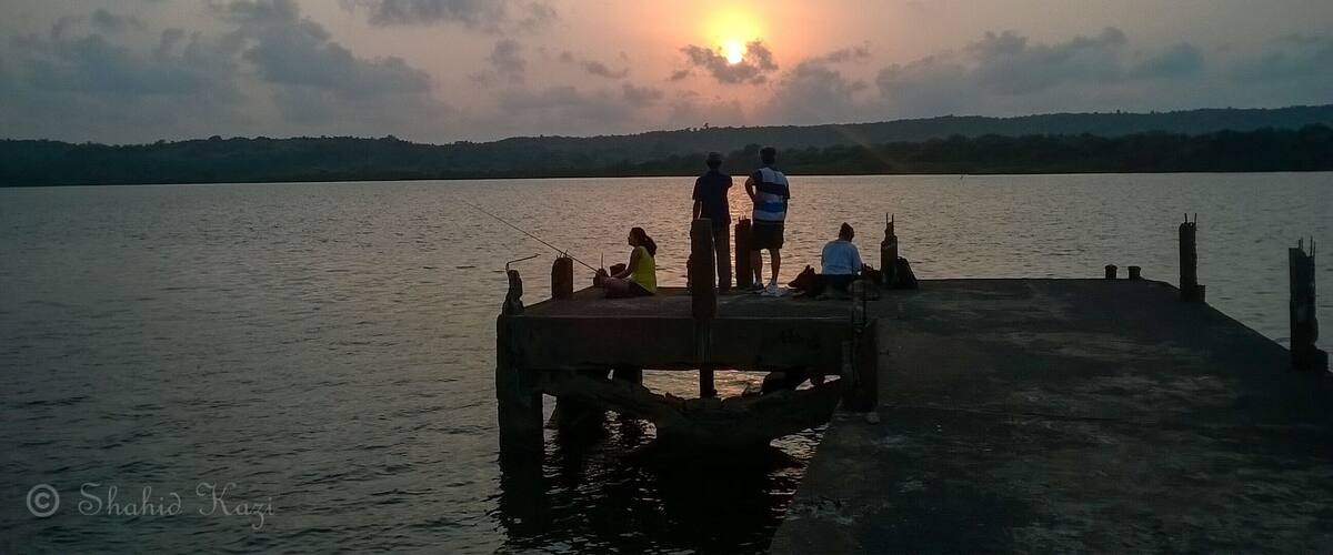 A sunset over a calm lake with people on a dock.