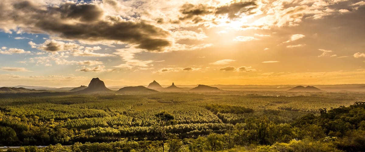 A landscape with a dense forest, rolling hills, and distant mountains under a partly cloudy sky.