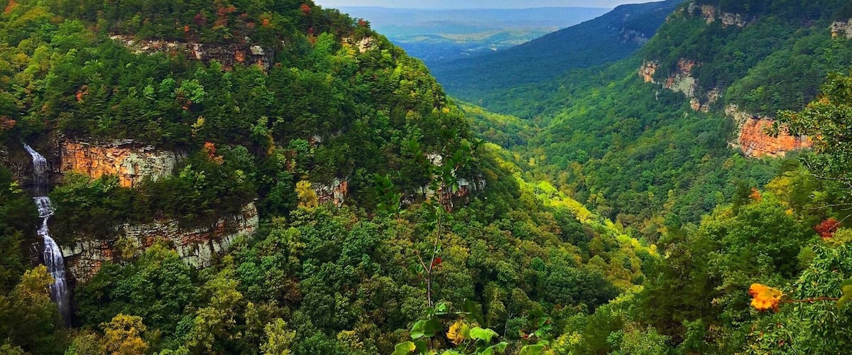 A lush valley with a waterfall and steep cliffs.
