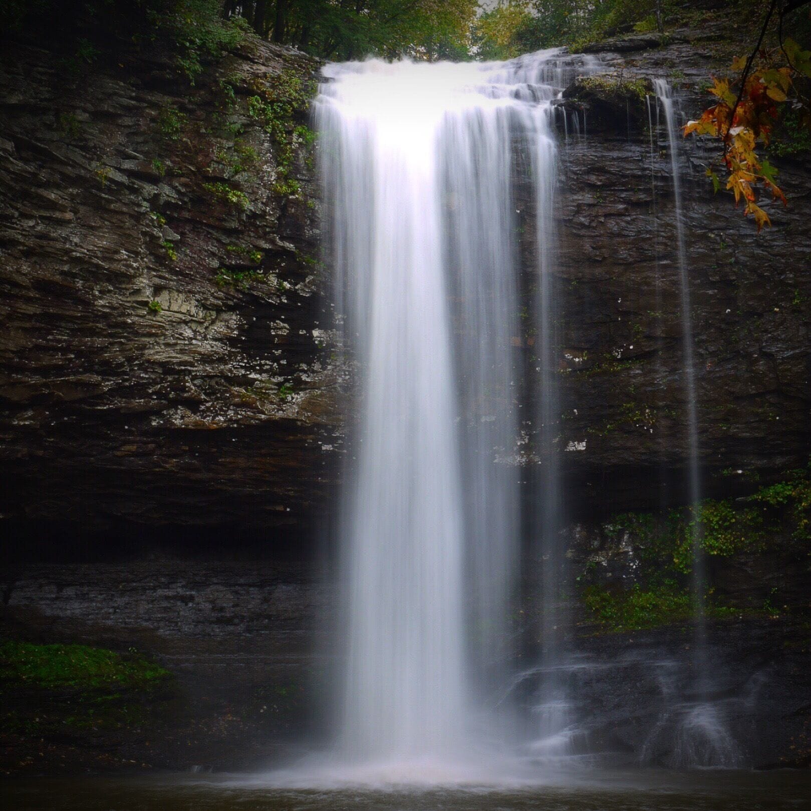 A waterfall cascading down a rocky cliff surrounded by greenery.