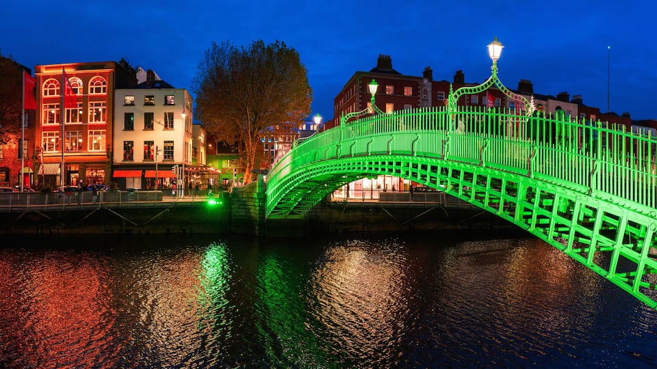 A green-lit bridge over water with buildings on either side.