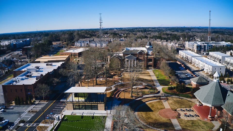 An aerial view of a town with a mix of modern and historic buildings, a central park, and a prominent clock tower.