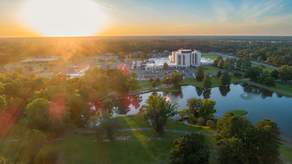 An aerial view of a campus with a large building, a lake, and surrounding greenery.