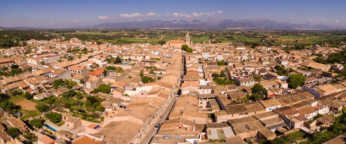 A panoramic view of a historic town with a prominent church tower, cobblestone streets, and surrounding green fields.