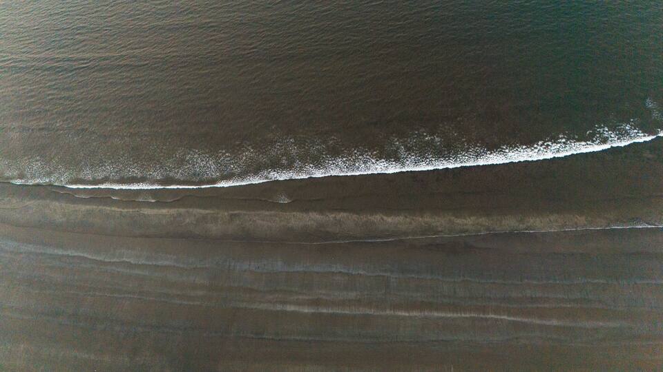 An aerial view of a beach with a visible wave breaking on the shore.