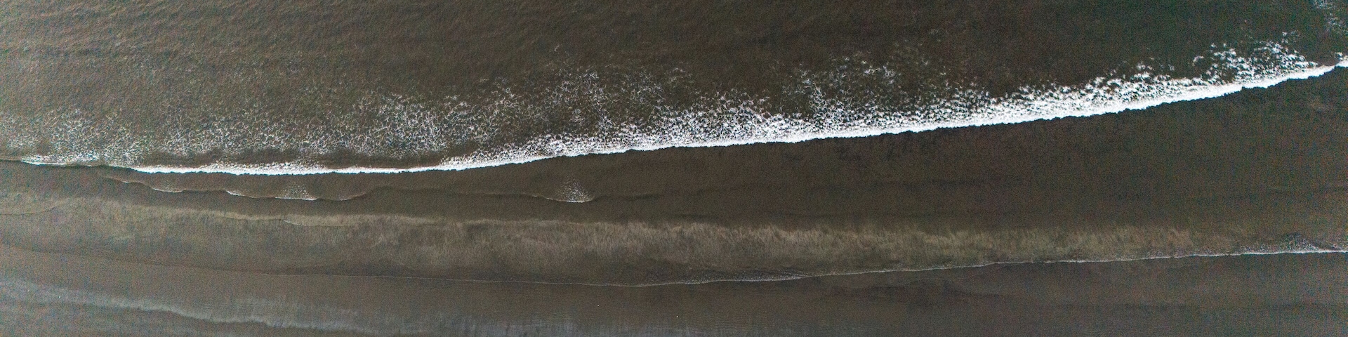 An aerial view of a beach with a visible wave breaking on the shore.