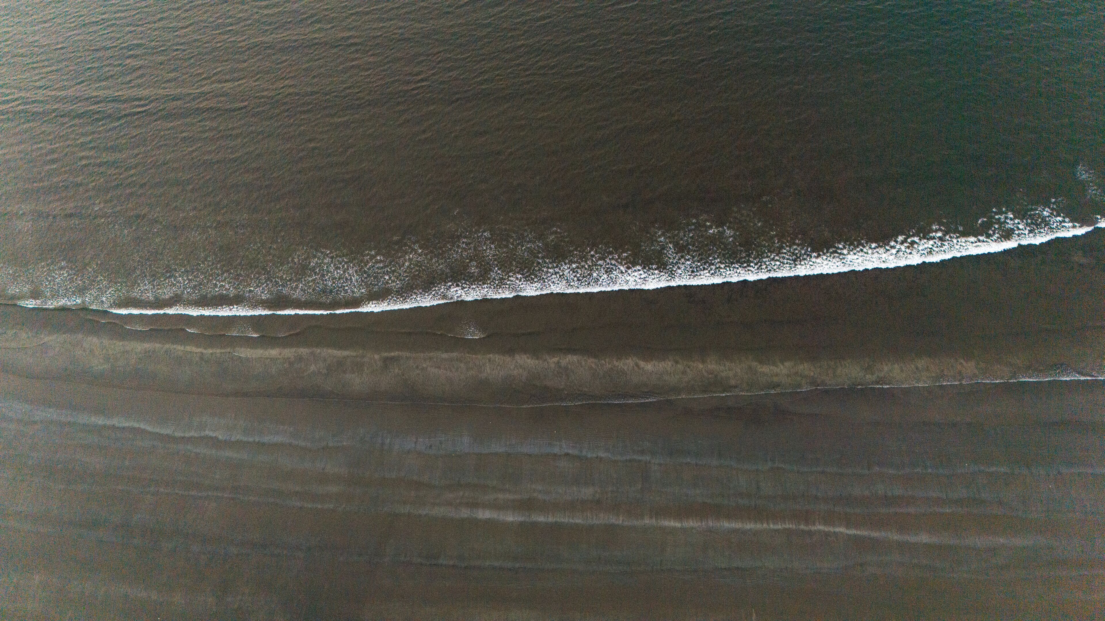 An aerial view of a beach with a visible wave breaking on the shore.