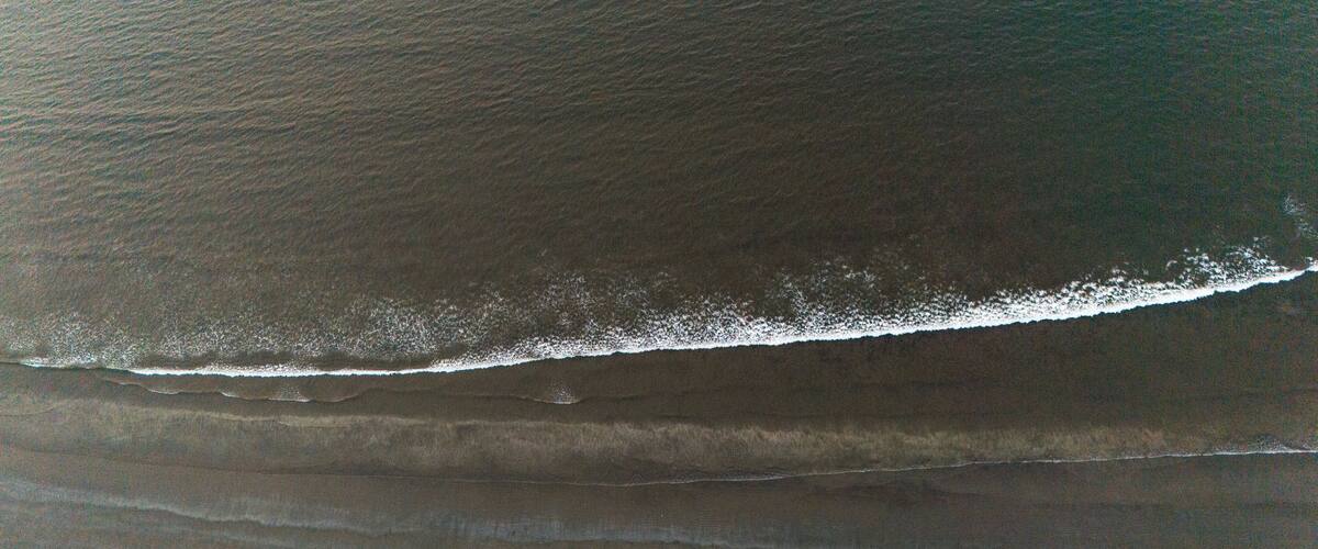 An aerial view of a beach with a visible wave breaking on the shore.