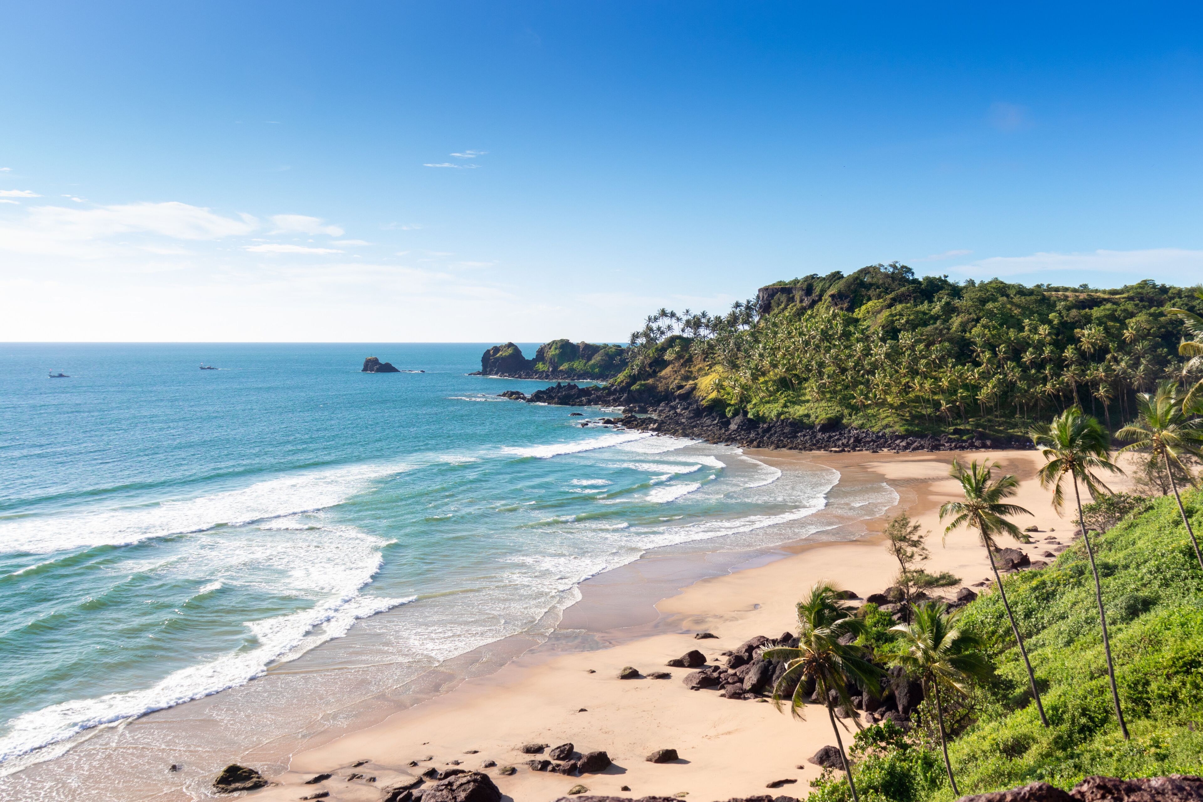 A tropical beach with clear blue waters, sandy shore, and lush green hills.