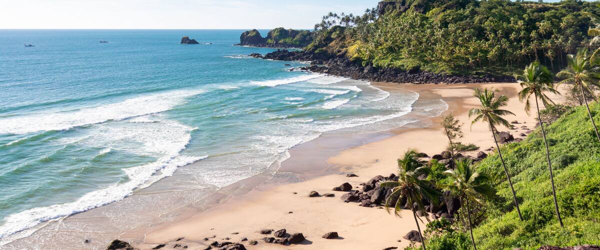 A tropical beach with clear blue waters, sandy shore, and lush green hills.
