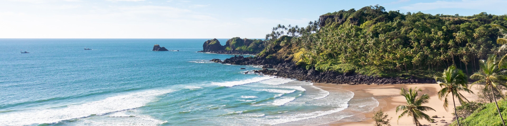 A tropical beach with clear blue waters, sandy shore, and lush green hills.