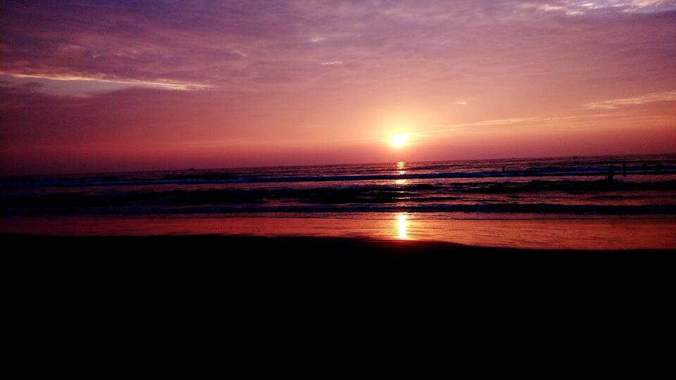 A sunset over the ocean with waves and a beach.