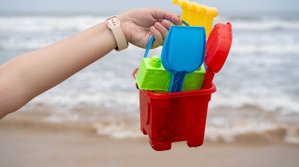 Woman holding up a colorful sand castle making kit with bucket, molds, shovel against the waves on baga, morjim, vagator, paolem beach in goa a popular tourist spot