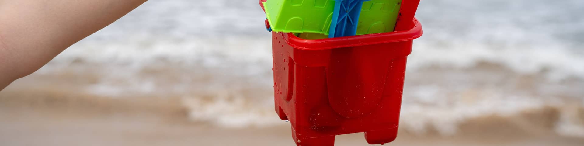 Woman holding up a colorful sand castle making kit with bucket, molds, shovel against the waves on baga, morjim, vagator, paolem beach in goa a popular tourist spot