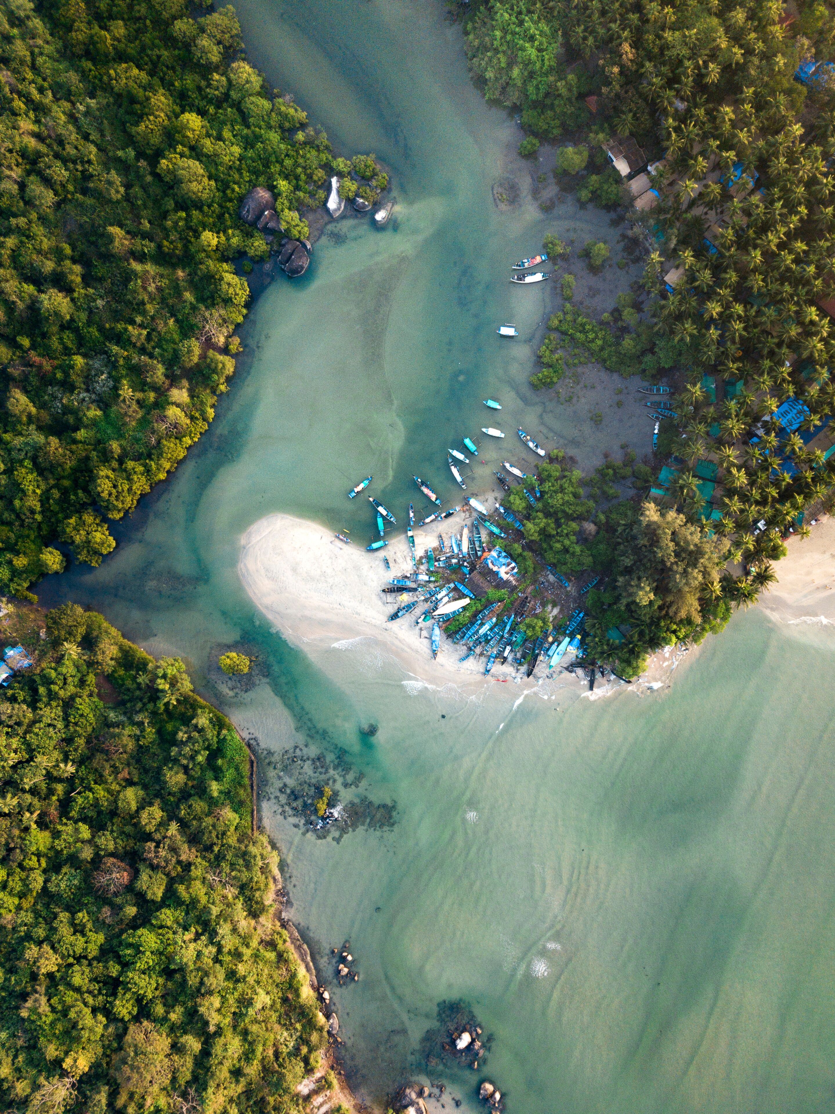 An aerial view of a coastal area with clear turquoise waters, a sandy beach, and numerous boats docked near the shore.