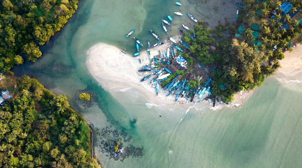 An aerial view of a coastal area with clear turquoise waters, a sandy beach, and numerous boats docked near the shore.