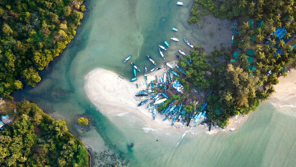 An aerial view of a coastal area with clear turquoise waters, a sandy beach, and numerous boats docked near the shore.