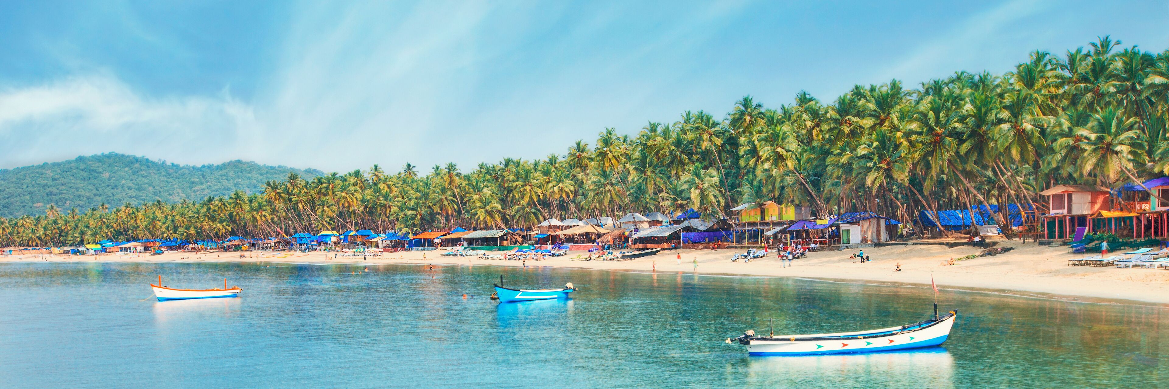 A beach with palm trees, boats, and beach huts.