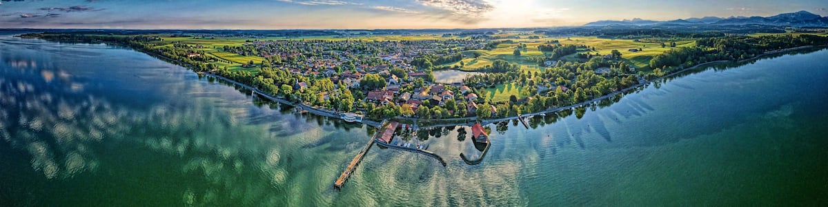Ein weiter Blick auf eine Stadt am Seeufer mit einer Brücke, Booten und umliegender Natur.