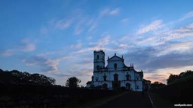 A white church with a bell tower and a dome, surrounded by trees and a stone wall.