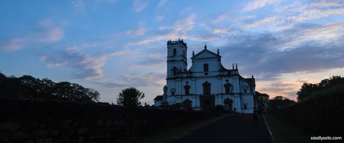 A white church with a bell tower and a dome, surrounded by trees and a stone wall.