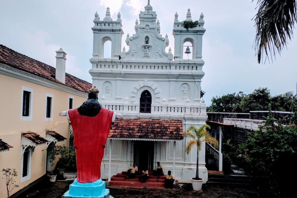 Una iglesia de estilo colonial blanco con dos torres de campanas y una estatua roja en primer plano.