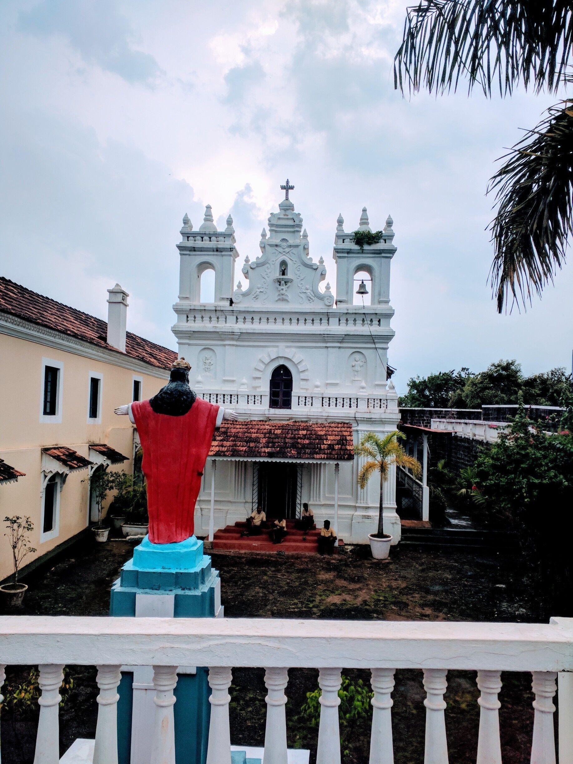 A white colonial-style church with two bell towers and a red statue in the foreground.
