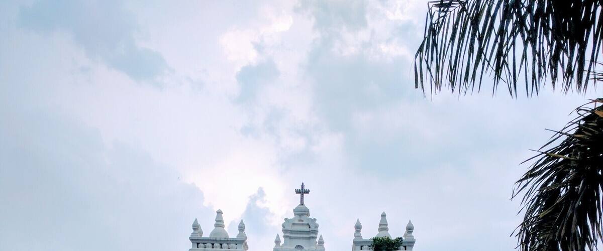 A white colonial-style church with two bell towers and a red statue in the foreground.
