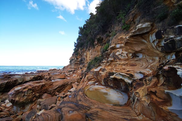 A coastal landscape with layered rock formations and a clear sky.