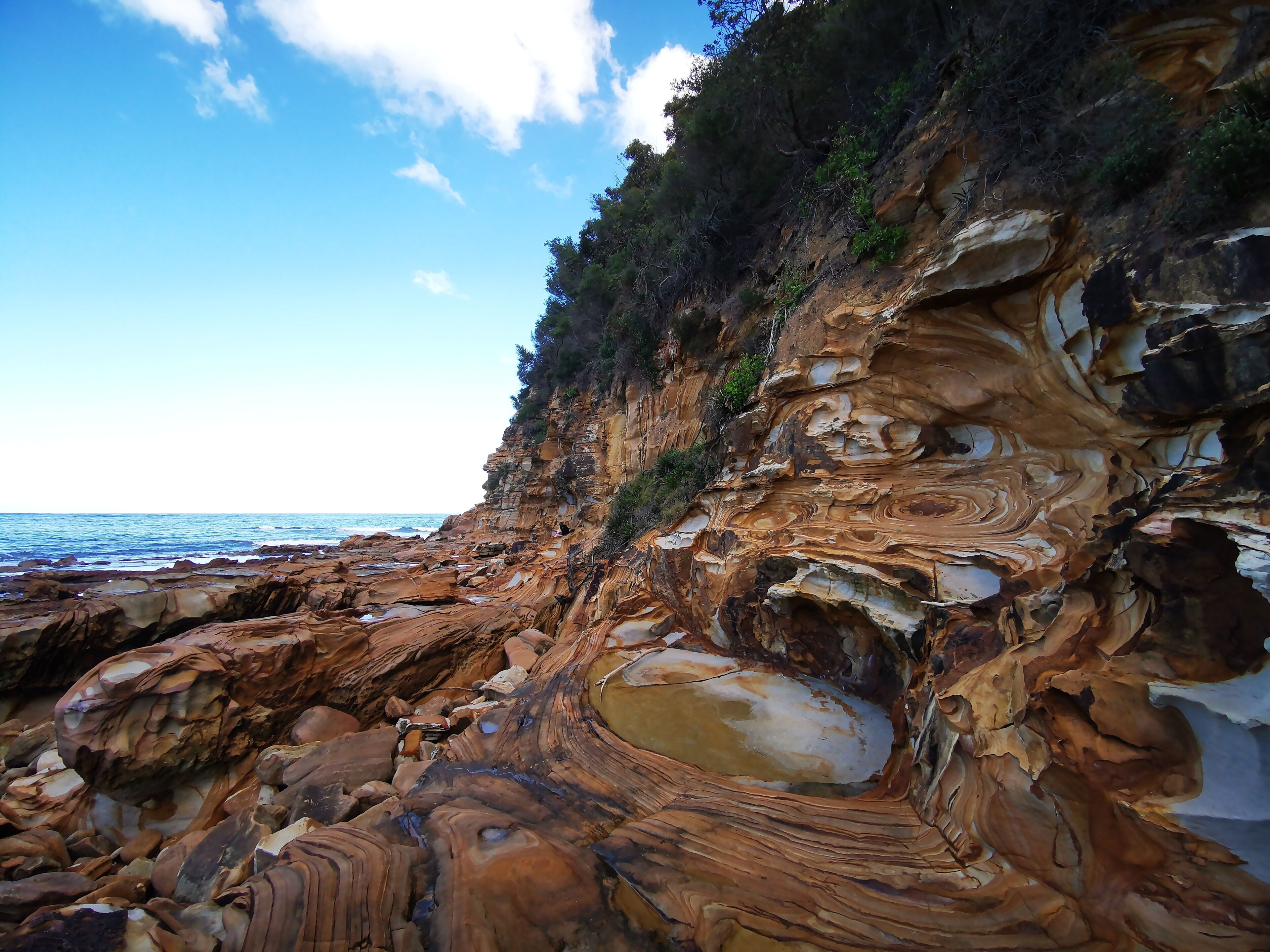 A coastal landscape with layered rock formations and a clear sky.