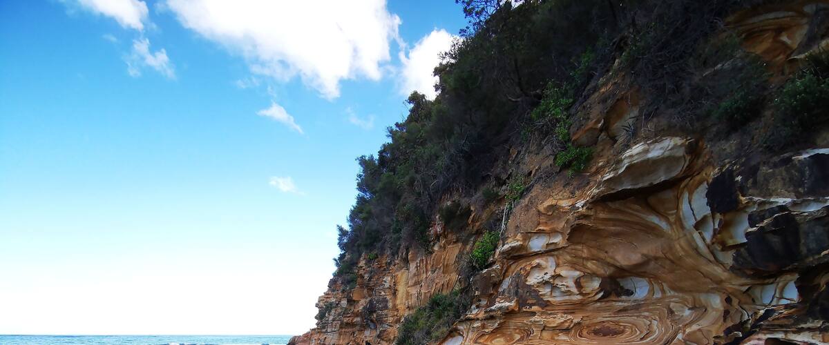 A coastal landscape with layered rock formations and a clear sky.