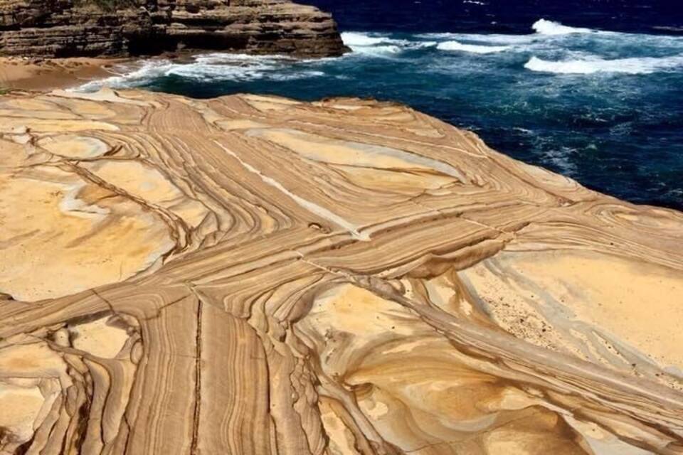 A coastal rock formation with layered patterns and the ocean in the background.