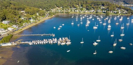 A marina with numerous sailboats docked, surrounded by a residential area and dense forest.
