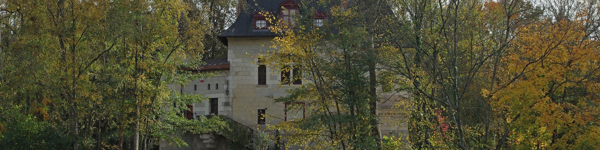 A historic castle surrounded by autumn foliage and a calm river.
