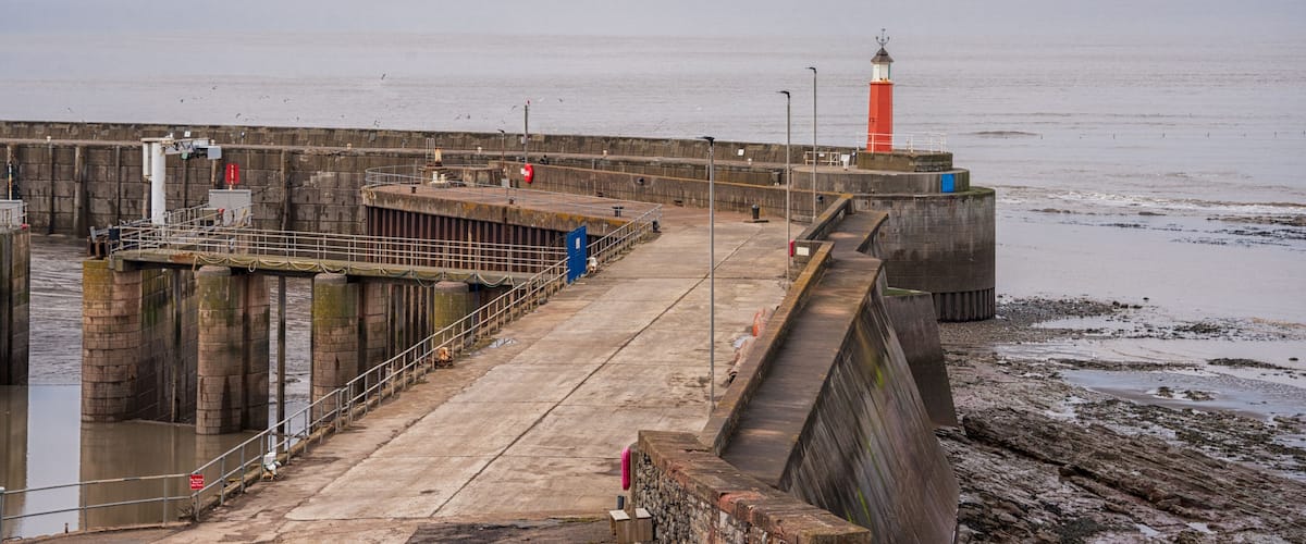 A pier with a lighthouse, stone walls, and a calm sea.