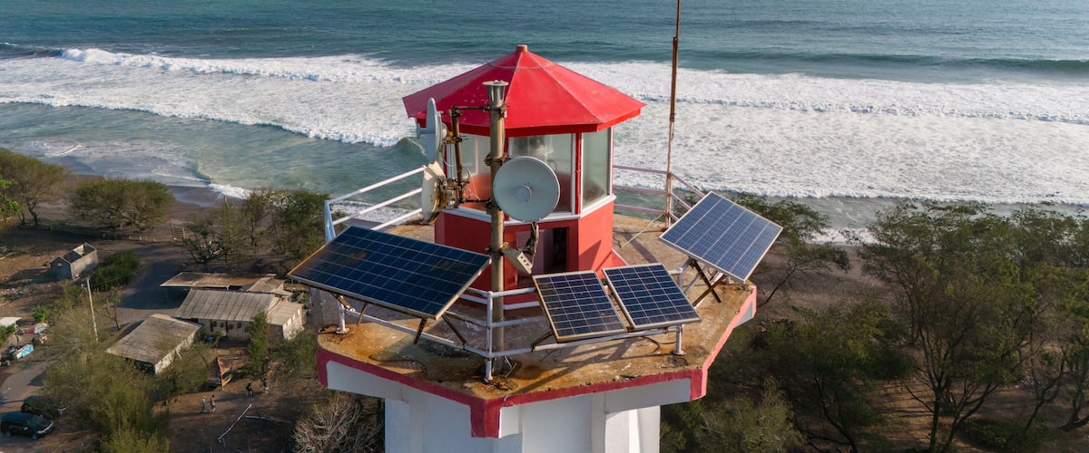 A red lighthouse with solar panels on a coastal cliff overlooking the ocean.