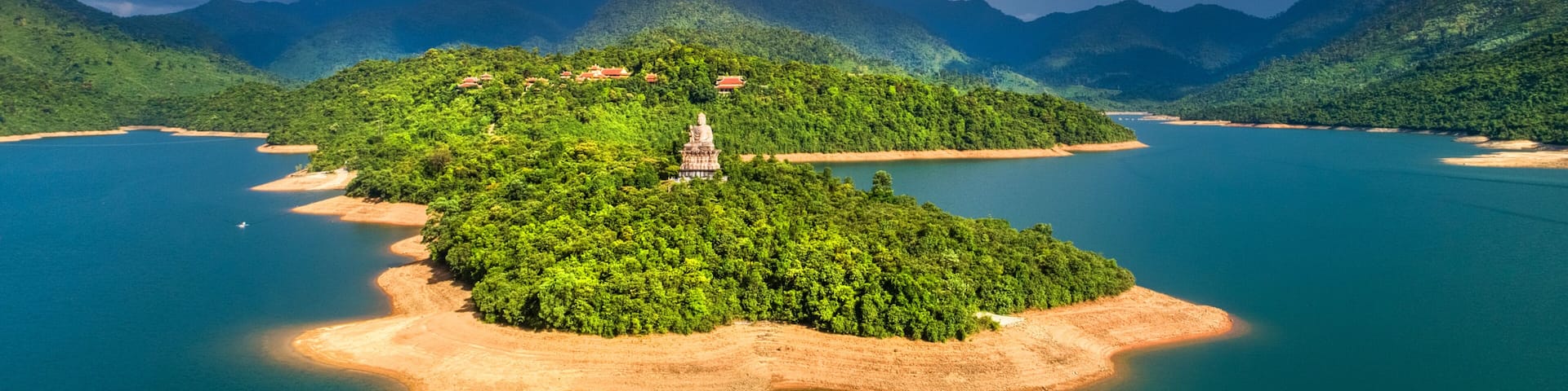 A lush green island with a temple in the center, surrounded by a calm blue lake and mountains in the background.